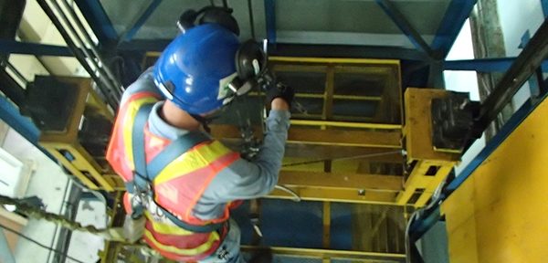 An LHESSA inspector in a hi-vis vest and hard hat examining the steel structure of an overhead crane