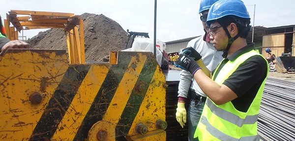 An inspector in a hi-vis vest examining the wear points on an excavator bucket